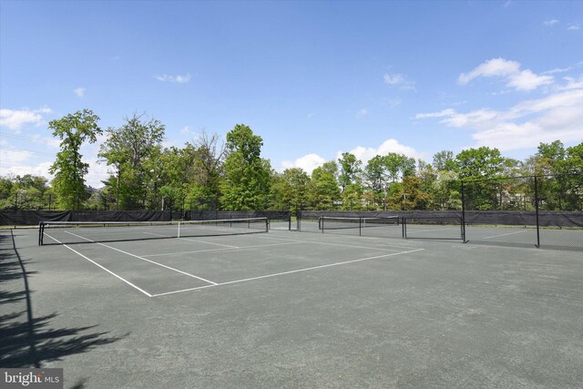view of tennis court with fence and view of wooded area
