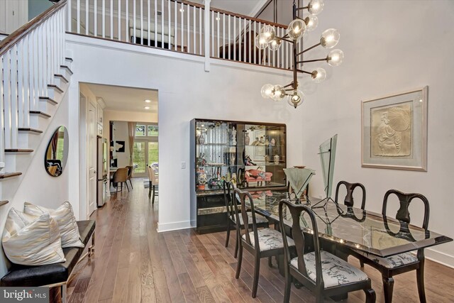 dining area with a high ceiling, stairway, wood finished floors, baseboards, and a chandelier