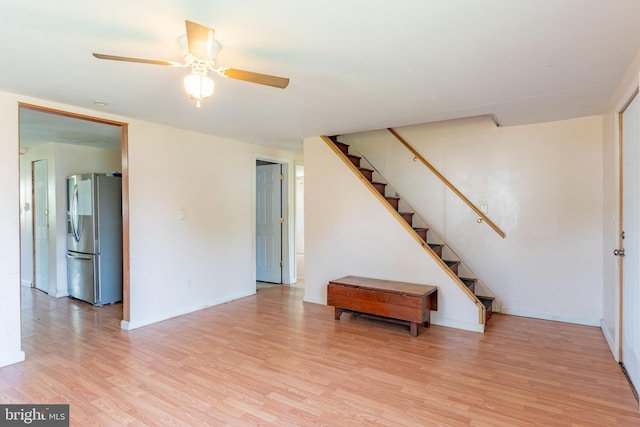 living area with light wood-style flooring, stairway, ceiling fan, and baseboards