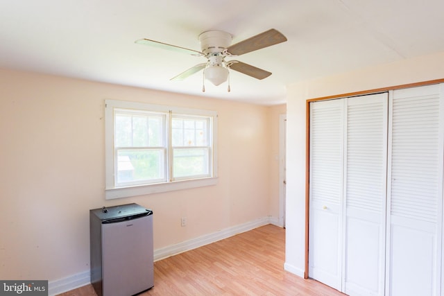 unfurnished bedroom with a closet, fridge, light wood-style floors, and baseboards