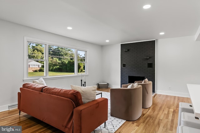 living area with light wood-style floors, recessed lighting, a brick fireplace, and baseboards