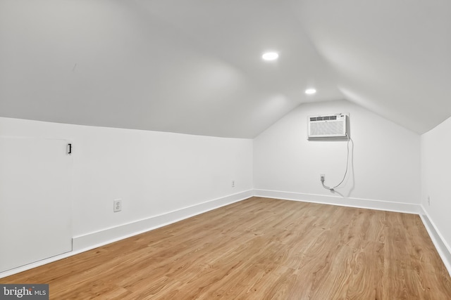 additional living space featuring vaulted ceiling, baseboards, light wood-style flooring, a wall unit AC, and recessed lighting