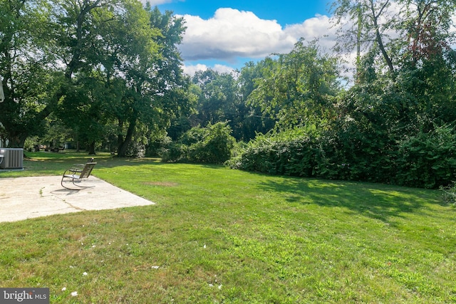 view of green lawn with central AC unit and a patio area