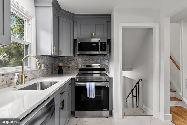 kitchen featuring appliances with stainless steel finishes, gray cabinetry, a sink, and tasteful backsplash