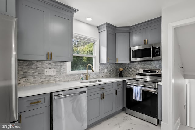 kitchen featuring appliances with stainless steel finishes, gray cabinets, a sink, and light marble finish floors