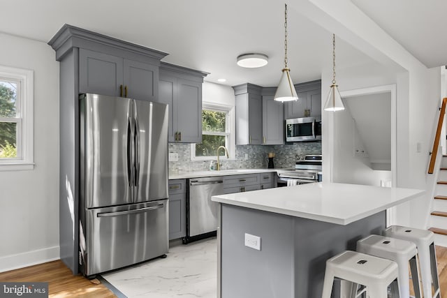 kitchen featuring stainless steel appliances, gray cabinetry, decorative backsplash, light countertops, and a kitchen bar