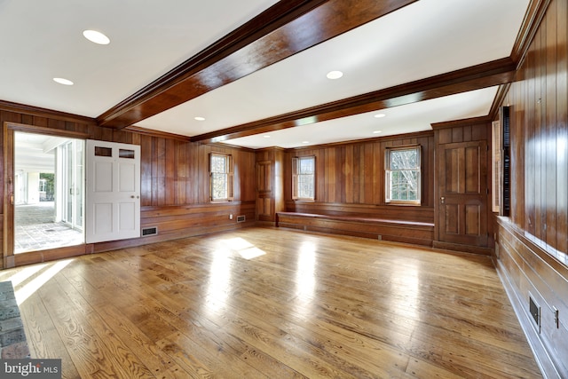 unfurnished living room featuring light wood finished floors, wooden walls, a healthy amount of sunlight, and beam ceiling