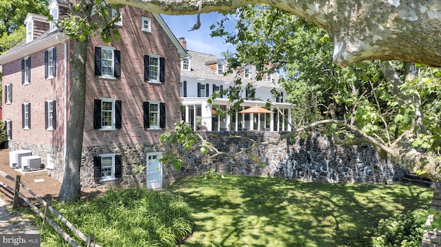 exterior space featuring a chimney, cooling unit, brick siding, and a front lawn