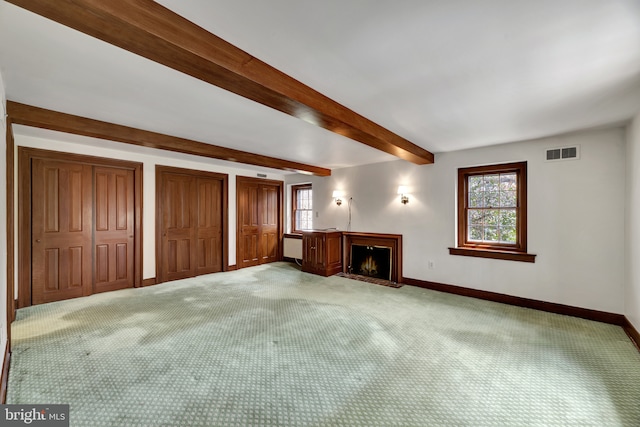 unfurnished living room with a healthy amount of sunlight, visible vents, light carpet, a lit fireplace, and baseboards