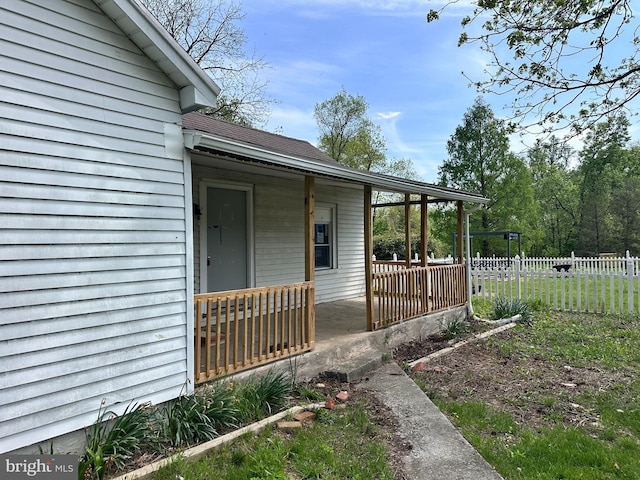 view of property exterior featuring a shingled roof, covered porch, and fence