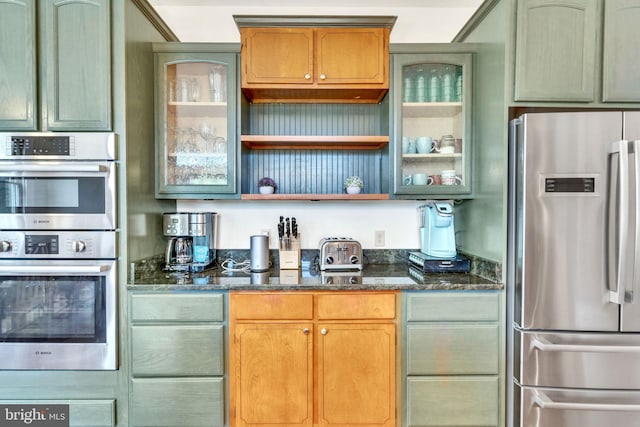 kitchen with glass insert cabinets, open shelves, dark stone countertops, green cabinetry, and appliances with stainless steel finishes