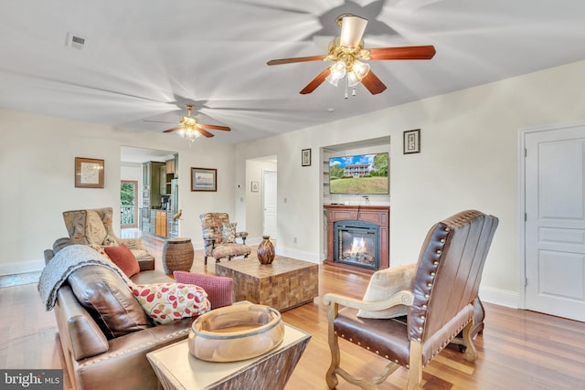 living area featuring light wood finished floors, baseboards, a ceiling fan, and a glass covered fireplace