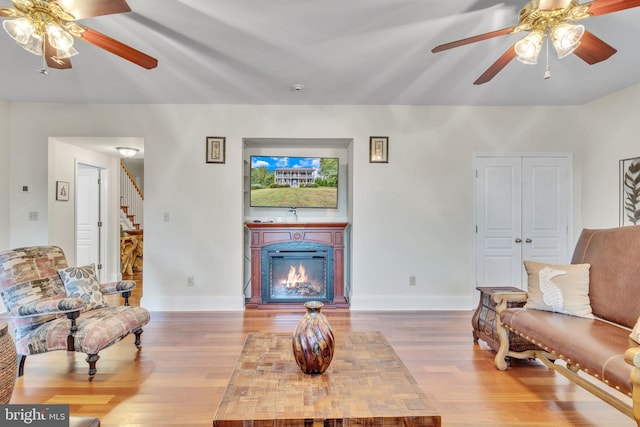 living area featuring stairway, ceiling fan, baseboards, and wood finished floors
