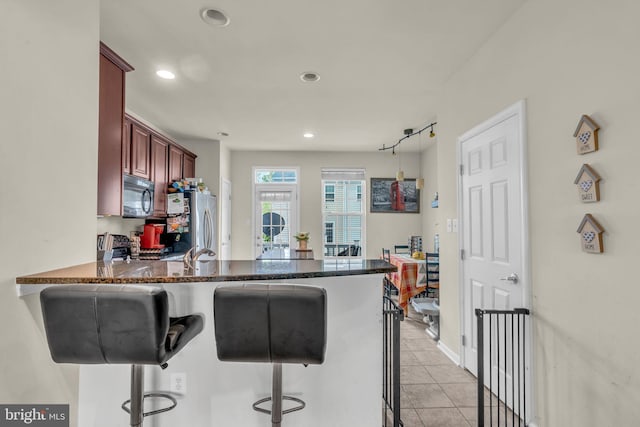 kitchen featuring a breakfast bar, freestanding refrigerator, a peninsula, and reddish brown cabinets