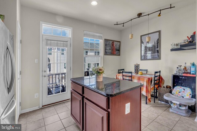 kitchen with freestanding refrigerator, a center island, decorative light fixtures, light tile patterned floors, and dark stone countertops