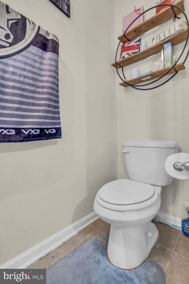 half bath with toilet, baseboards, and tile patterned flooring