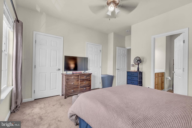 bedroom featuring ensuite bath, light colored carpet, baseboards, and ceiling fan