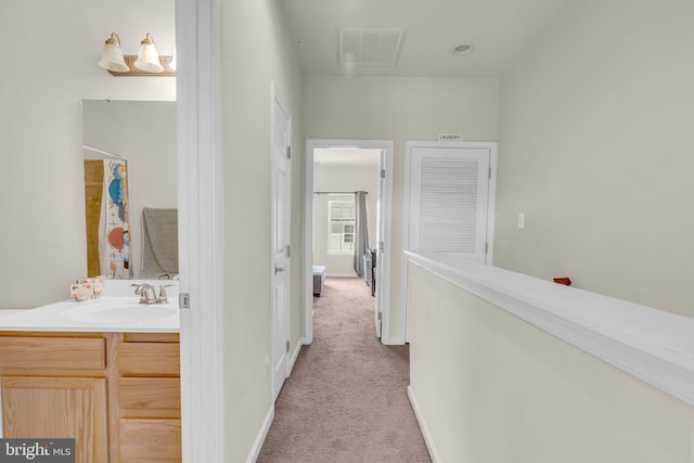 hallway featuring a sink, attic access, visible vents, baseboards, and light carpet