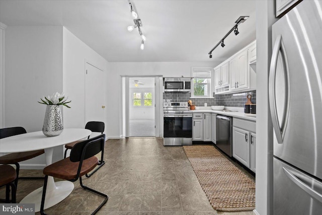 kitchen featuring baseboards, track lighting, decorative backsplash, light countertops, and appliances with stainless steel finishes