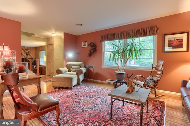 living area with stairway, light wood-type flooring, a baseboard heating unit, and baseboards