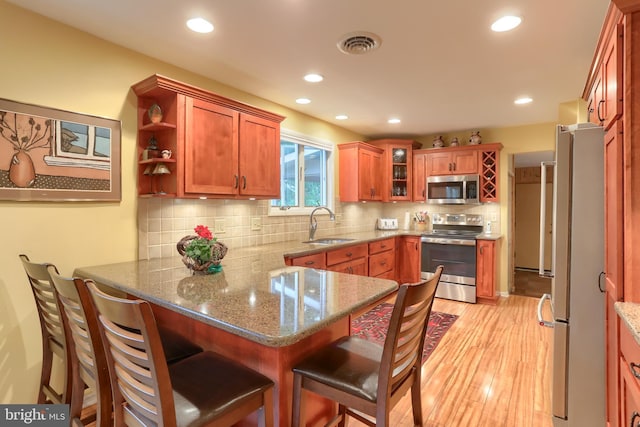 kitchen with stainless steel appliances, a peninsula, a sink, light wood finished floors, and light stone countertops
