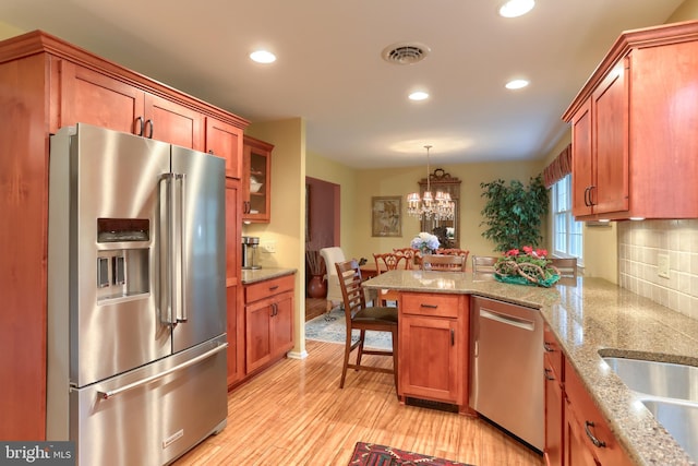kitchen featuring stainless steel appliances, a peninsula, recessed lighting, brown cabinetry, and decorative light fixtures