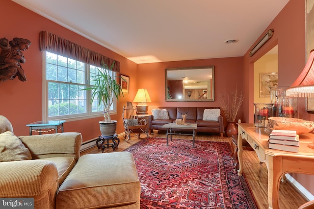 living room with a baseboard heating unit, wood finished floors, and baseboards