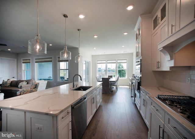 kitchen with a sink, a kitchen island with sink, white cabinetry, dark wood-type flooring, and appliances with stainless steel finishes