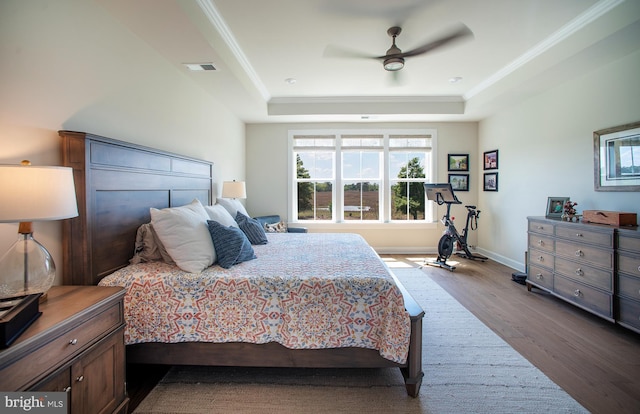bedroom with a tray ceiling, crown molding, dark wood-type flooring, baseboards, and visible vents