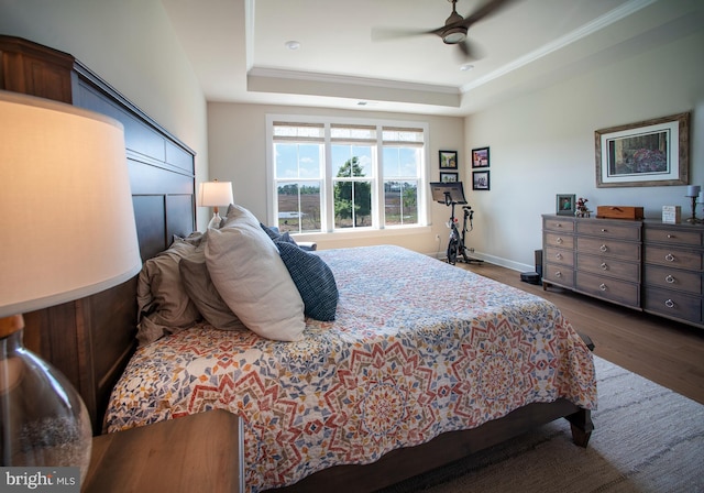 bedroom featuring a tray ceiling, crown molding, dark wood-type flooring, baseboards, and ceiling fan