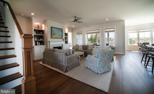 living room featuring a fireplace, stairs, dark wood-type flooring, and a ceiling fan