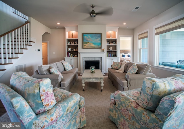 carpeted living room with a ceiling fan, stairway, a premium fireplace, and visible vents