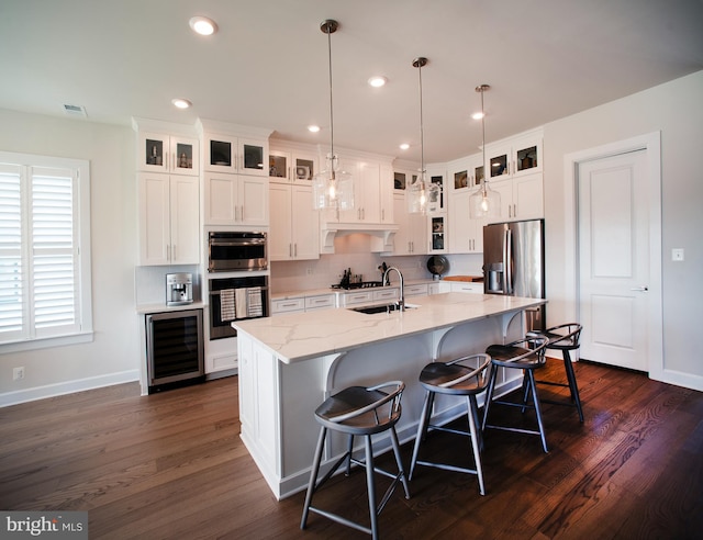 kitchen with a sink, a kitchen island with sink, white cabinetry, appliances with stainless steel finishes, and wine cooler