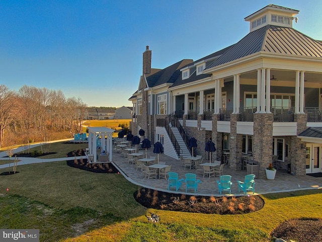 rear view of house featuring a yard, a patio area, a standing seam roof, and a chimney