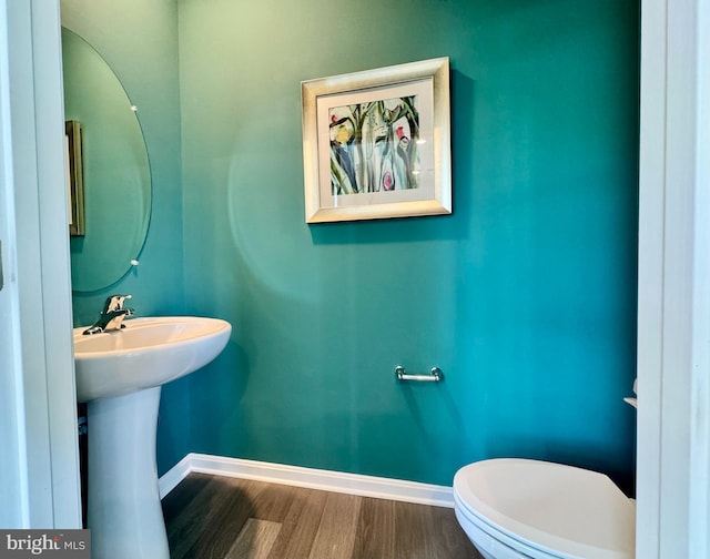 half bath with baseboards, toilet, and wood finished floors