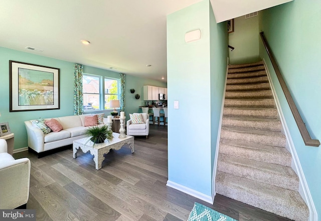 living area featuring baseboards, stairs, visible vents, and wood finished floors