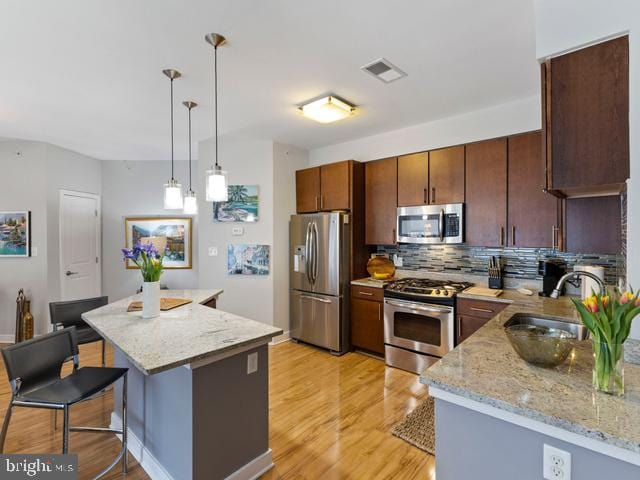 kitchen with a sink, light wood-type flooring, visible vents, appliances with stainless steel finishes, and decorative backsplash