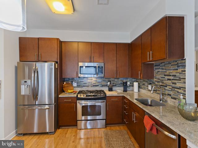 kitchen with light stone counters, a sink, light wood-style floors, tasteful backsplash, and appliances with stainless steel finishes