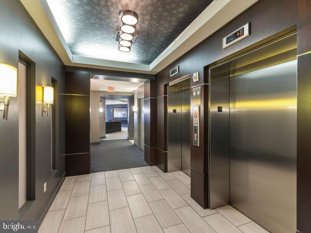 hall featuring a tray ceiling, elevator, and carpet