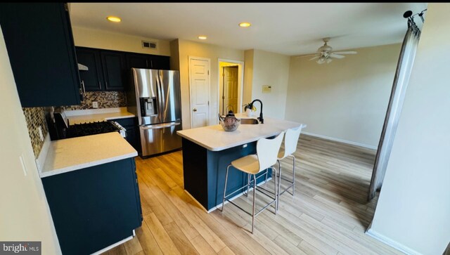 kitchen with stainless steel fridge, dark cabinets, gas range, light countertops, and a breakfast bar