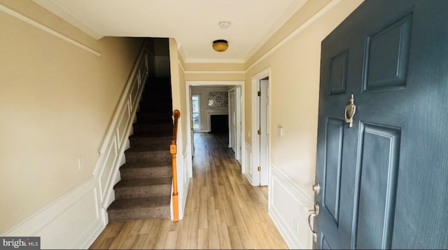 entryway featuring light wood finished floors, stairs, a decorative wall, and crown molding