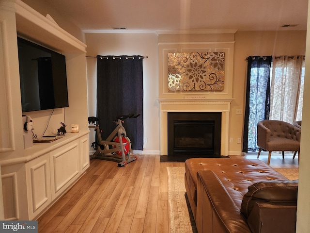 living room featuring light wood-style flooring, crown molding, and a fireplace with flush hearth