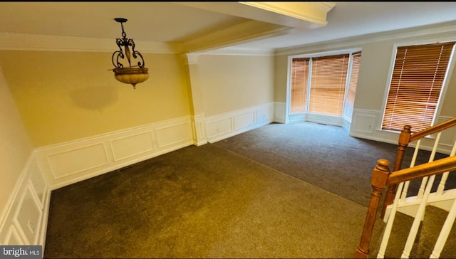 empty room featuring dark carpet, a decorative wall, crown molding, stairs, and wainscoting