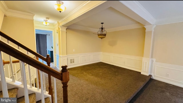 empty room featuring dark colored carpet, crown molding, decorative columns, stairs, and a wainscoted wall