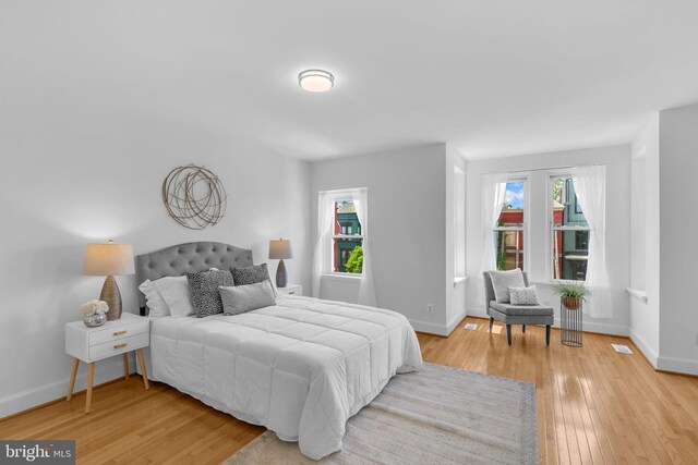 bedroom with multiple windows, light wood finished floors, and baseboards