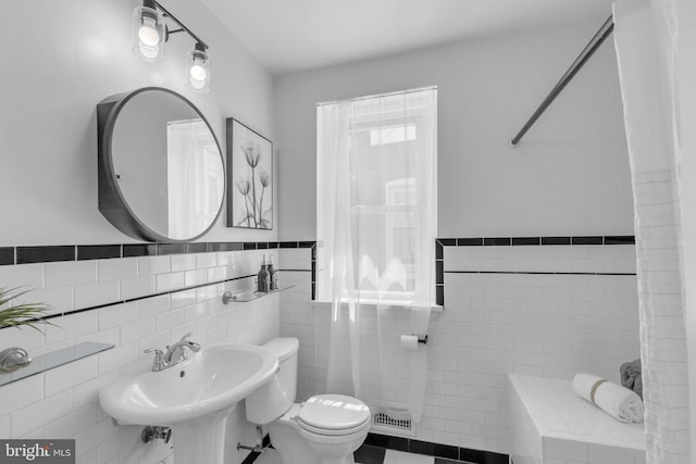 bathroom with tile walls, toilet, a wainscoted wall, a sink, and tile patterned flooring