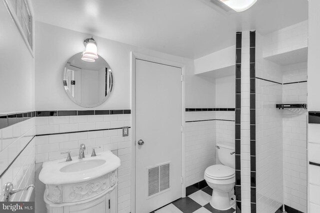full bathroom with tile walls, toilet, a wainscoted wall, vanity, and a shower