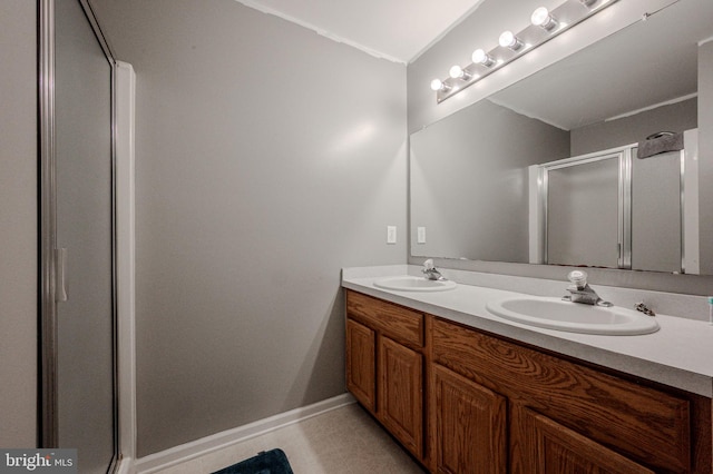 bathroom featuring a stall shower, baseboards, double vanity, and a sink