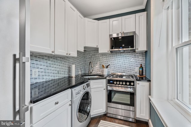kitchen with washer / clothes dryer, stainless steel appliances, a sink, dark countertops, and white cabinetry
