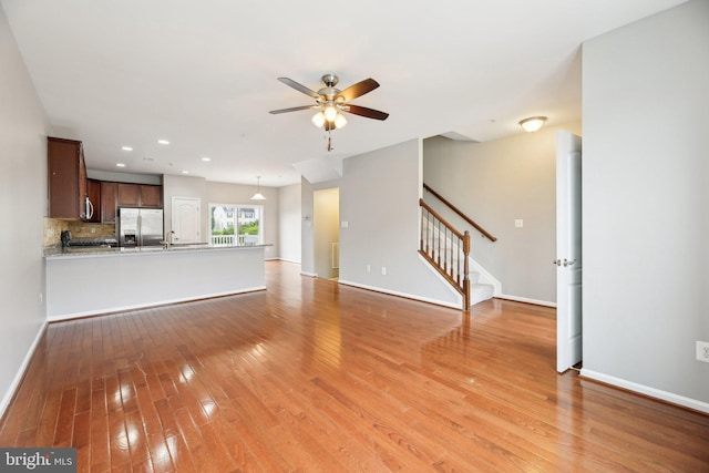 unfurnished living room featuring ceiling fan, light wood finished floors, stairway, baseboards, and a sink